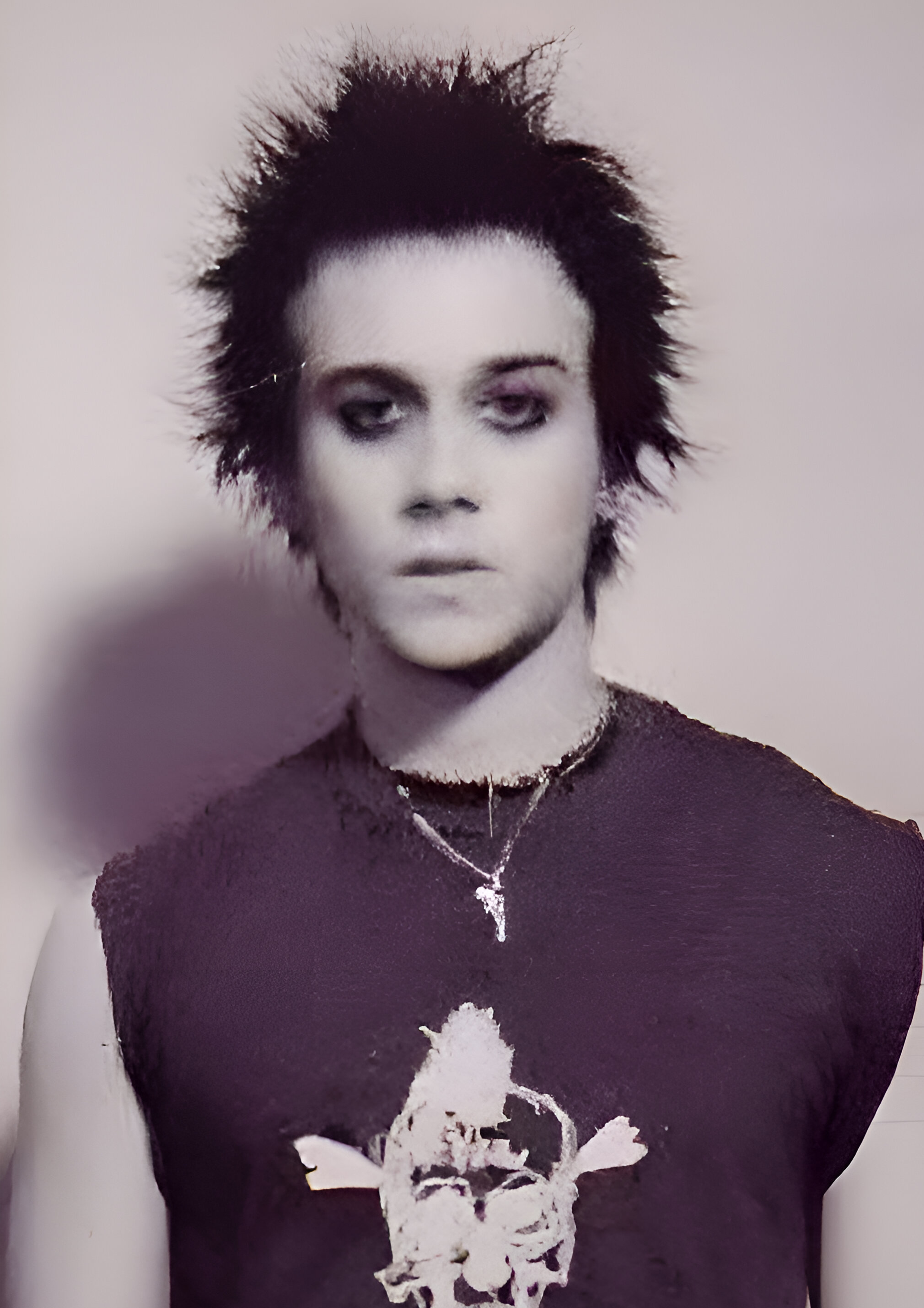 Before image: An image in the style of a police mugshot of punk young adult with spiky black hair, wearing a black tank top with a skull on it, called the 'Jesus Of Suburbia' staring at the camera.
